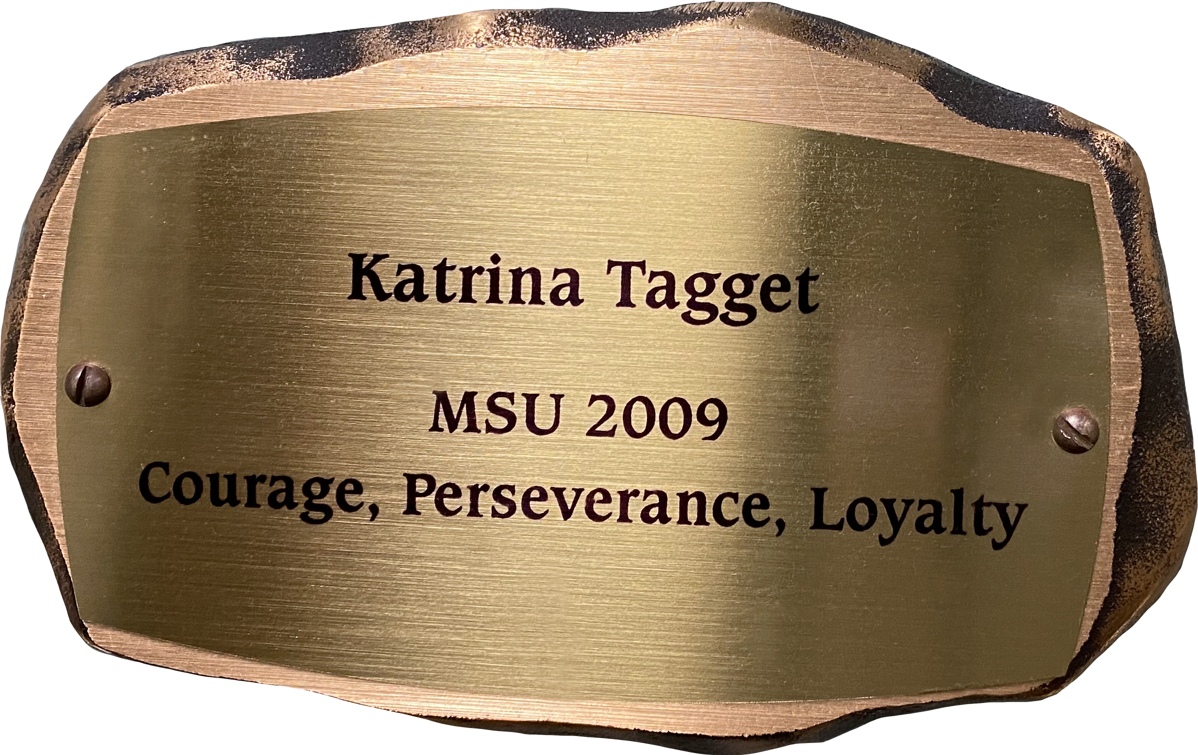 Inscribed bronze plaque in the shape of a rock with text on it reading: "Katrina Tagget MSU 2009 Courage, Perseverance, Loyalty"