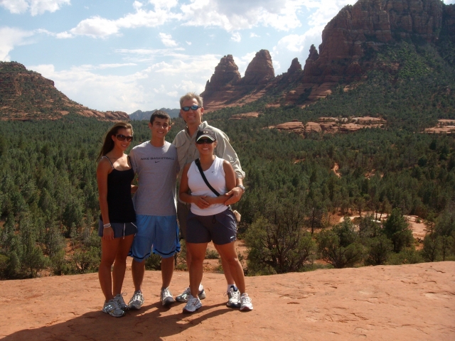 The Powell family standing high on a mountain with orange sand, overlooking a green valley