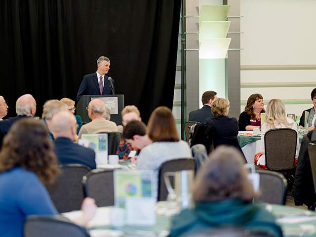 RCPD Director Michael Hudson at the podium during a recent Awards Reception, with a crowd of attendees watching him
