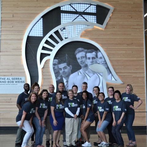 RCPD Staff posed together in matching t-shirts in front of Spartan Helmet in the Breslin Center.