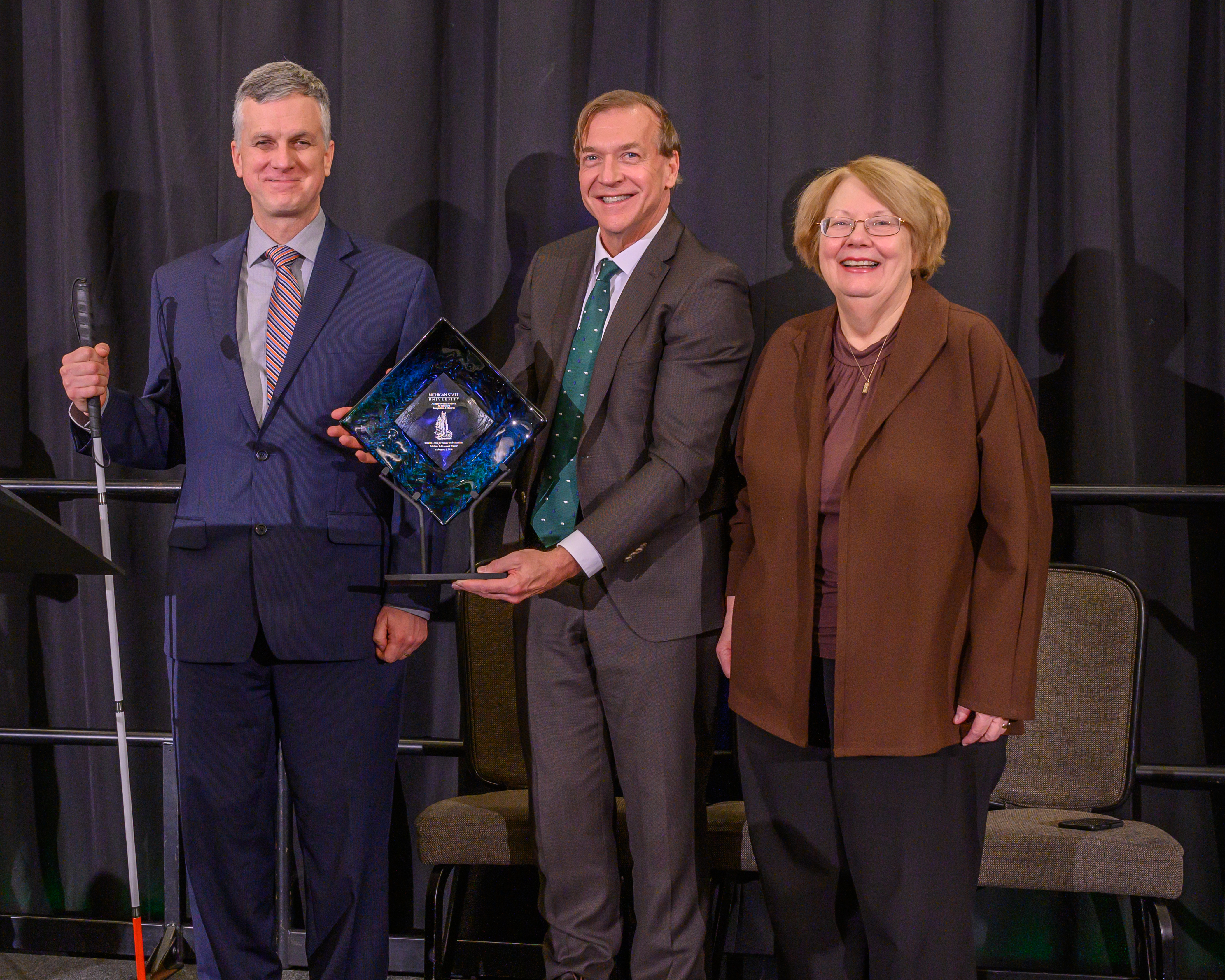 Michael Hudson holds the Crystal Award with President Stanley and Provost Sullivan