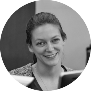 A black and white photo of Becca smiling behind a computer. Becca as a Caucasian woman