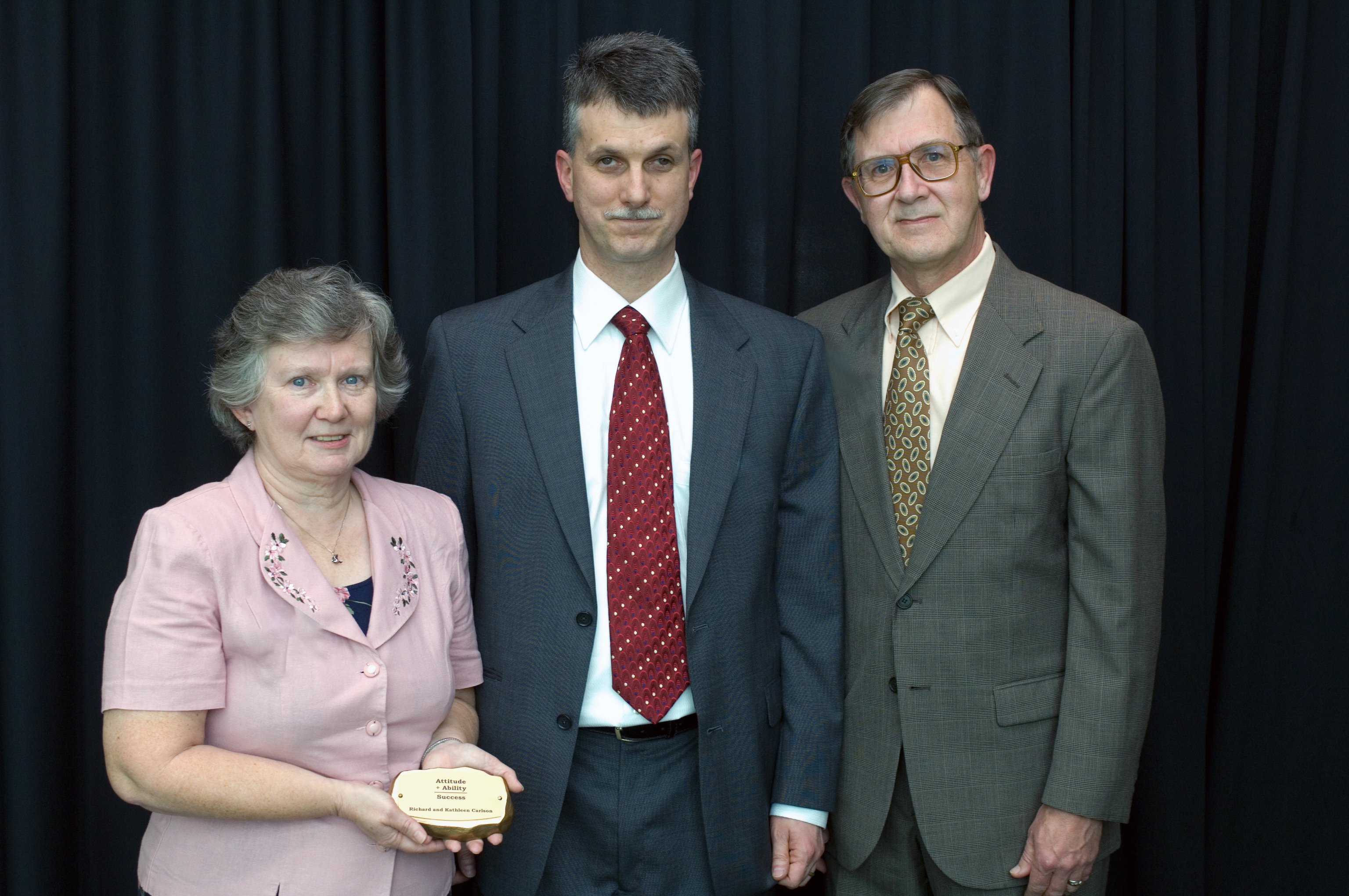 Richard and Kathleen Carlson posing with Michael Hudson as he presents them with their commemorative rock.