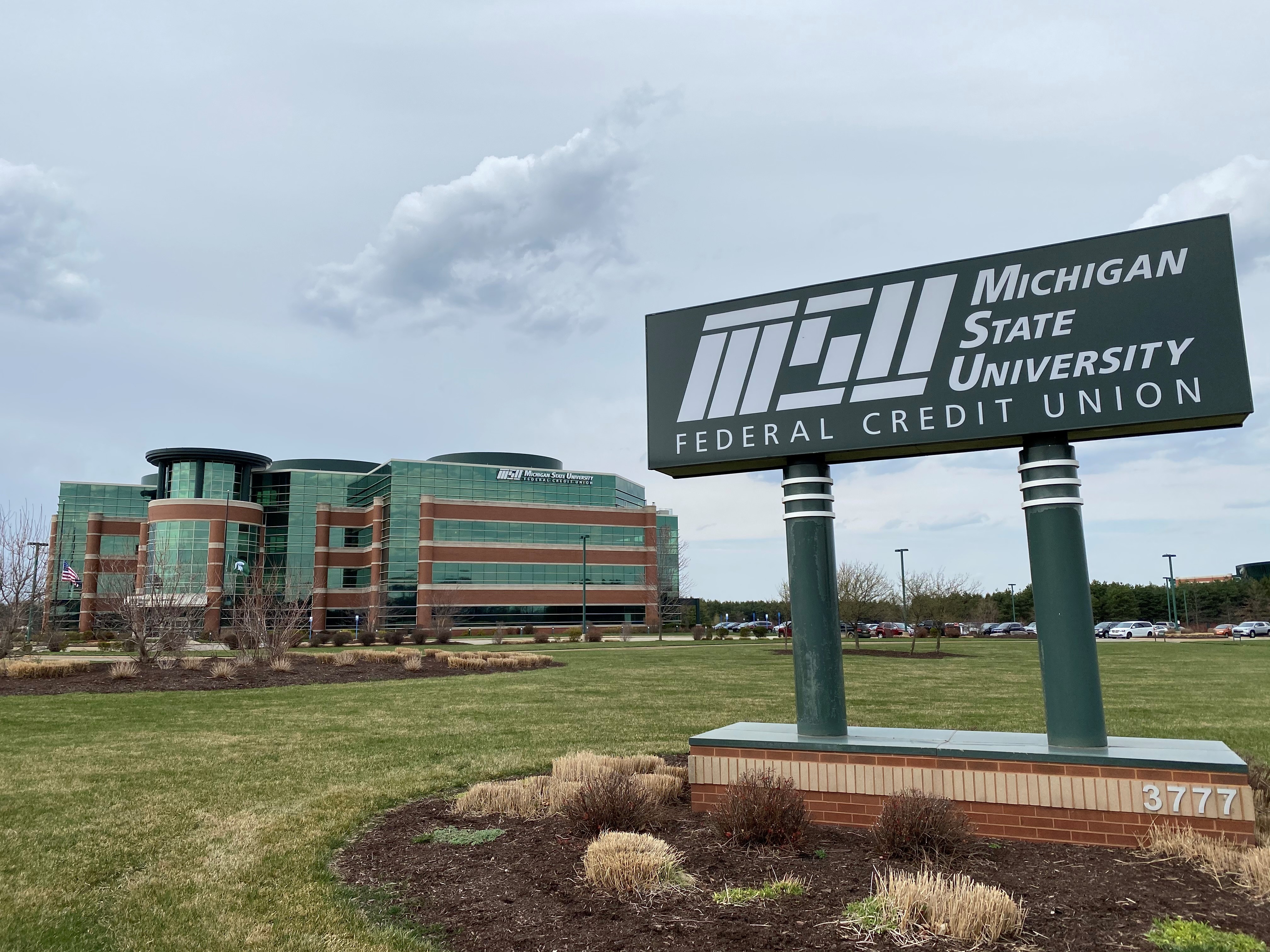MSUFCU main office building in the background with a large green MSUFCU sign in the foreground