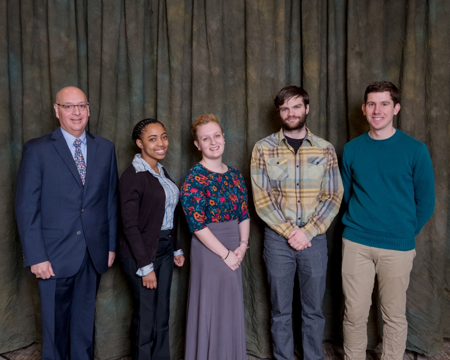 Five formally-dressed individuals pose for a photo in front of a grey background