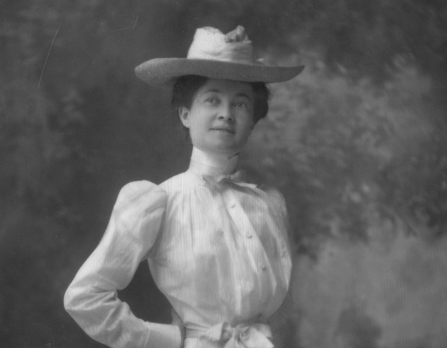 Black and white photo of young May Shaw wearing a white dress and a hat