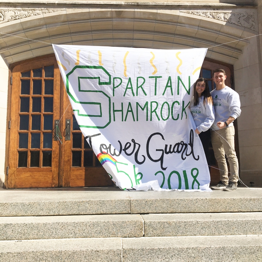 Jenna Kesh standing in front of MSU Auditorium with 2018 Shamrock Banner