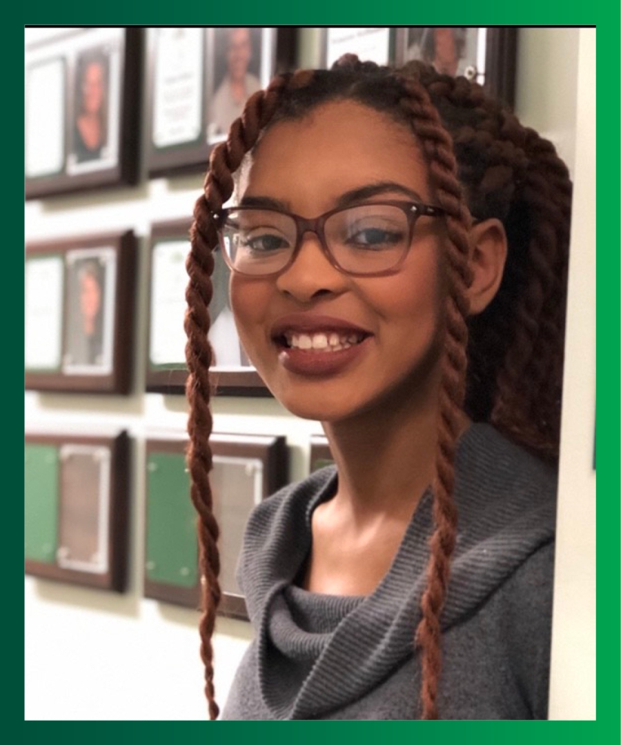 Picture of Jasmine J., smiling Black female, with box braids in ponytail, wearing grey turtleneck sweater and glasses.