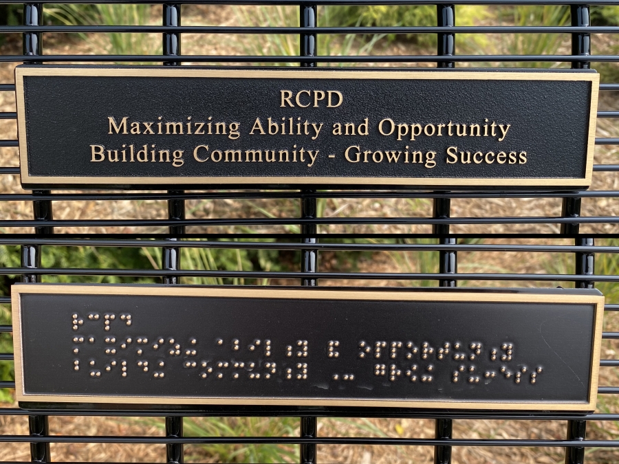 Close up photos of the seating plaques, one in print and one in braille, which read "RCPD Maximizing Ability and Opportunity Building Community - Growing Success"