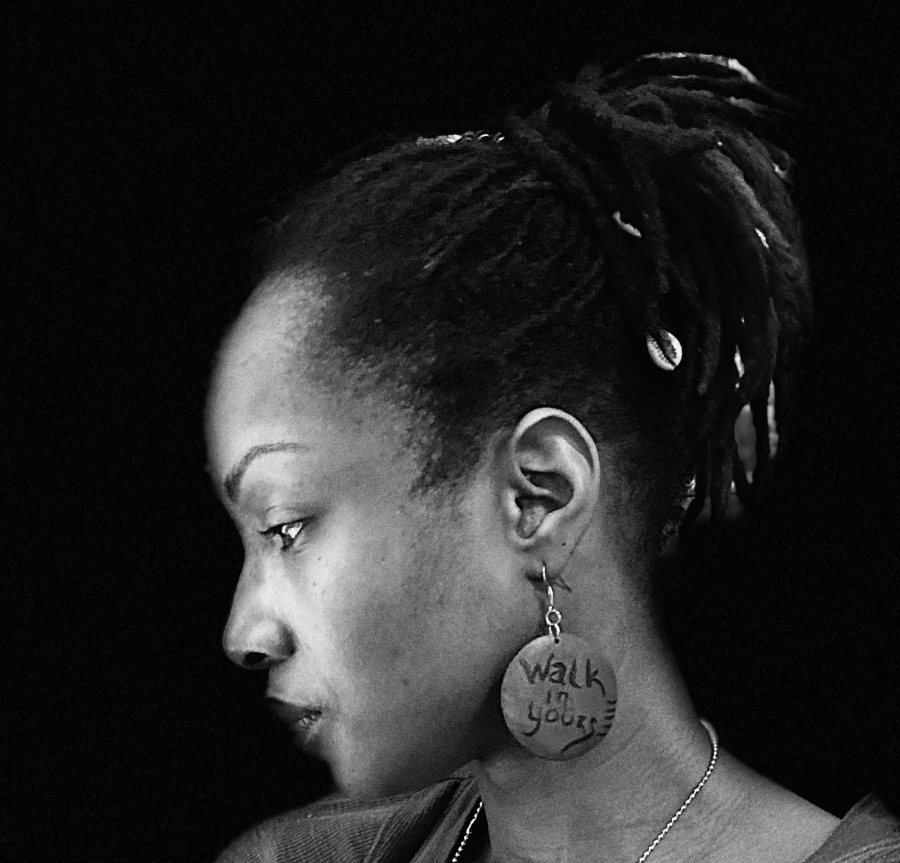 Photographed is Leah Ellis, a Black woman with locs, placed in a ponytail, and dangling earrings.