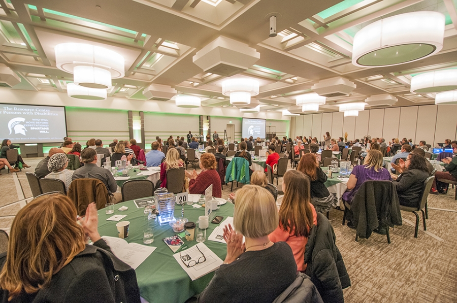 A picture of the reception space within Kellogg Center. Guests are seated at tables and clapping 