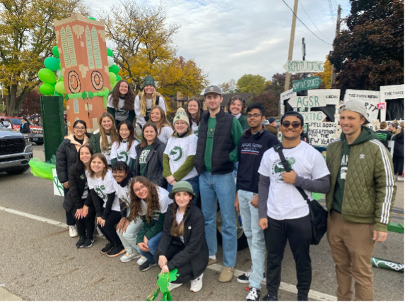 Tower Guard members smile at the camera in front of their Homecoming Float during the parade, featuring a cardboard version of Beaumont Tower and a Lucky Charms theme.