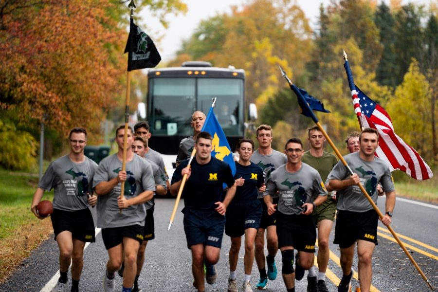 Runners carrying a US flag on a wet fall day with a Dean's Trailway bus following behind