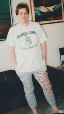 Photo of Philip Trosko standing infront of a couch wearing a Michigan State University t-shirt and the University of Wisconsin sweatpants