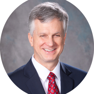 Photo of Michael Hudson, smiling light skinned man with short, salt and pepper hair, wearing a blue sport coat and white dress shirt with a red tie. Click for biographical details. 