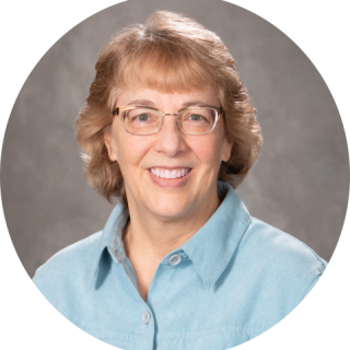 Photo of Virginia (Ginger) Martz, a smiling light skinned woman with short brown hair. She is wearing a blue blouse, and eye glasses. Click for biographical details. 