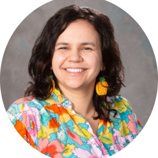 Photo of Lynne Swerhone, a woman with collar-bone length brown hair smiling at the camera, wearing a brightly colored patterned shirt.